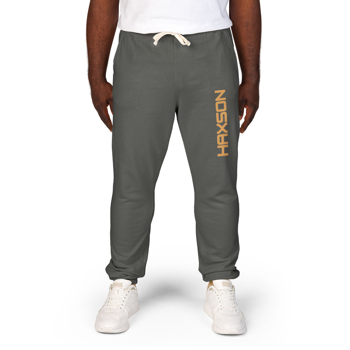 A person wearing dark gray sweatpants with a vertical orange 'HAXSON' logo on the left leg, styled with a white t-shirt and white sneakers against a plain white background.